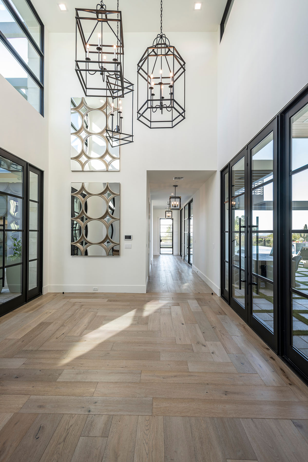 A sunlit entry hall by Trish Bowman Design featuring large-scale pendant lighting, patterned wall mirrors, and warm wood flooring for a welcoming first impression.