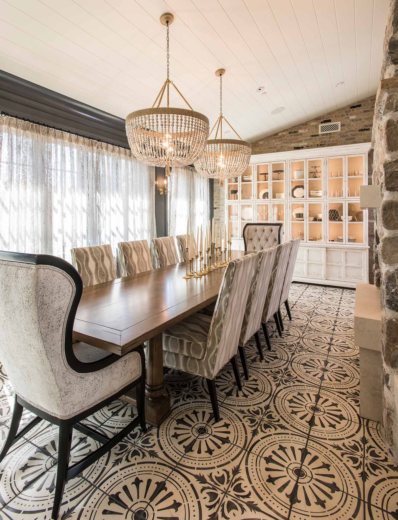 A transitional-style dining room by Trish Bowman Design, featuring patterned tile flooring, soft neutral tones, and oversized beaded chandeliers for a touch of rustic elegance.