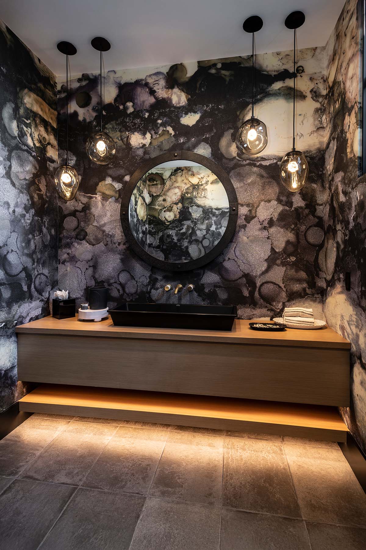 Bold powder room design by Trish Bowman Design with artistic black and gray wallpaper, ambient pendant lighting, and a custom floating wood vanity.
