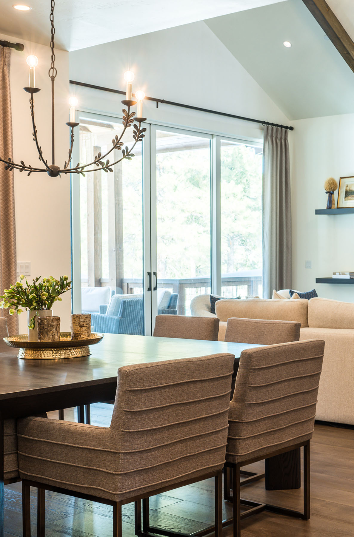The dining table centerpiece includes birch-wrapped candles and a potted green arrangement on a gold tray beneath an iron chandelier.